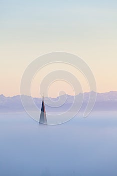 Churchtower above the fog, swiss alps in background