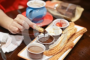 Churro. A hand holding a piece of Churro dipping in a dark chocolate sauce. Selective focus photo