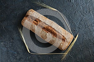 Ciabatta bread on a black background with ears of rye and wheat, top view