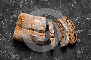 Ciabatta. Dark fresh healthy flattish open-textured Italian bread on black rustic background. Close-up. Top view