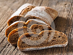 Ciabatta. Dark fresh healthy flattish open-textured Italian bread with a floury crust on wooden background. Close-up