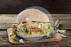 Ciabatta sandwich with chicken breast, cheese and green salad close up on the wooden background