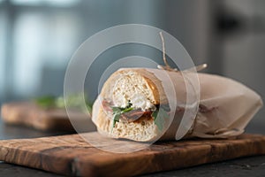 Ciabatta sandwich with salame, arugula, red pesto and cream cheese wrapped in paper on olive board photo