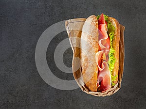 Ciabatta wrapped in papaer with prosciutto and vegetables on dark background
