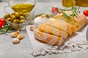 Ciabattas, olive oil in a bowl with olives, herbs, spices, garlic, pesto, parmesan and ciabatta bread on a texture background.