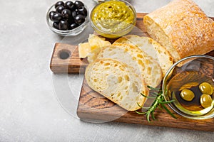 Ciabattas, olive oil in a bowl with olives, herbs, spices, garlic, pesto, parmesan and ciabatta bread on a texture background.