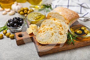 Ciabattas, olive oil in a bowl with olives, herbs, spices, garlic, pesto, parmesan and ciabatta bread on a texture background.