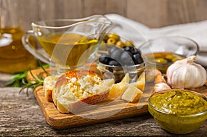 Ciabattas, olive oil in a bowl with olives, herbs, spices, garlic, pesto, parmesan and ciabatta bread on a texture background.