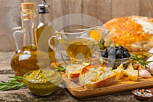 Ciabattas, olive oil in a bowl with olives, herbs, spices, garlic, pesto, parmesan and ciabatta bread on a texture background.