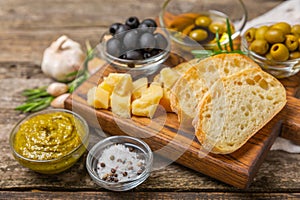 Ciabattas, olive oil in a bowl with olives, herbs, spices, garlic, pesto, parmesan and ciabatta bread on a texture background.