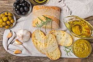 Ciabattas, olive oil in a bowl with olives, herbs, spices, garlic, pesto, parmesan and ciabatta bread on a texture background.