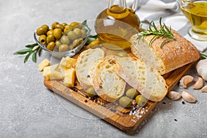 Ciabattas, olive oil in a bowl with olives, herbs, spices, garlic, pesto, parmesan and ciabatta bread on a texture background.