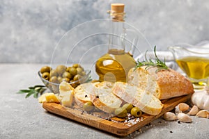 Ciabattas, olive oil in a bowl with olives, herbs, spices, garlic, pesto, parmesan and ciabatta bread on a texture background.