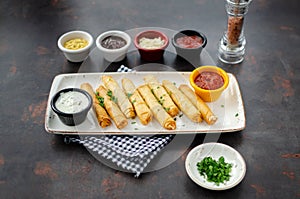 Cigarette Borek in white porcelain plate with various sauces on dark background