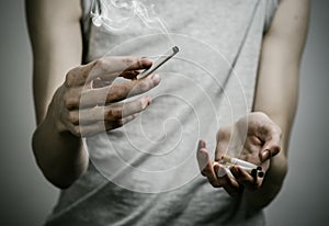 Cigarettes, addiction and public health topic: smoker holds the cigarette in his hand and a red heart on a dark background in the