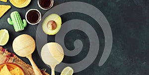 Cinco de Mayo-inspired flat lay featuring maracas, tequila shots, lime, nacho chips, avocado on a dark vintage background photo