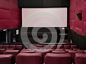 Cinema - interior of a movie theatre with empty red and black seats with white screen