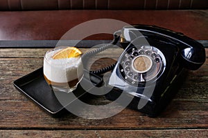 Cinema style photo of black dial phone and coffee cocktail with orange peel on wooden table. Luxury, creative background, Old fash photo