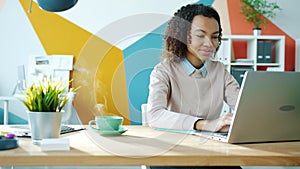 Cinemagraph loop of beautiful Afro-American girl using laptop in office with hot drink on table