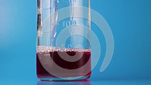 Cinemagraph of pink liquid poured into a glass measuring bottle on a deep blue background