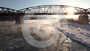 Cinematic Drone Shot, Flies Forward Over the Frozen River and Under the Red Steel Bridge at Sunrise, Aerial 4k Footage