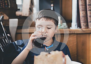 Cinematic Happy young boy drinking glass of cold drink, Portrait Child  sitting in cafe or coffee shop drinking soda or soft drink