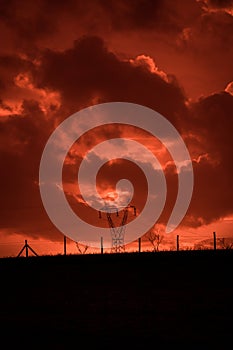 Scary sunset, with red sky and clouds, after storm. Power pylons and industrial fences in devastated landscape. B Evil environment