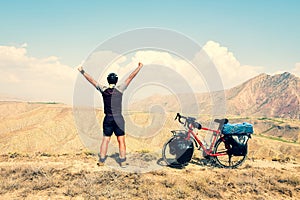 Cinematic inspirational excited fit caucasian male cyclist stand on top viewpoint by red touring bicycle in deserted mountains