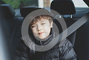 Cinematic portrait boy siting in safety car seat looking at camera with smiling face,Child sitting in the back passenger seat with