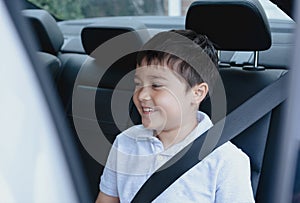 Cinematic portrait boy siting in safety car seat looking out with smiling face,Child sitting in the back passenger seat with a