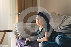 Cinematic Portrait of young boy lying on sofa watching TV in living room, Kid holding remote control, Child llies on couch looking