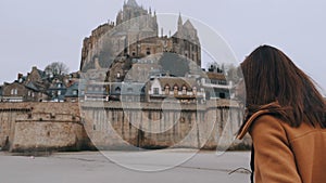 Cinematic rear view on stylish blogger woman walking to stunning Mont Saint Michel castle landmark in France slow motion