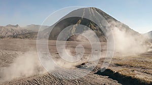 Cinematic shot aerial view of motocross rider driving in a volcanic dusty desert near beautiful Mount Bromo in East Java