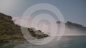 Cinematic shot of tourists in raincoats watching epic wall of water at beautiful famous Niagara waterfall on sunny day.