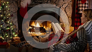 Cinematic shot of young woman reading book and relaxing cozy burning fireplace