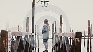 Cinematic wide shot of happy beautiful woman with camera enjoying perfect travel moments on romantic Venice gondola pier