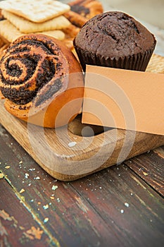 Cinnamon bun and chocolate muffin on a wooden backdrop with empty business card template