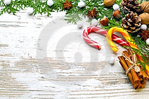 Cinnamon, caramel a hook, nuts, an anisetree, fir-tree branches, snow on a light wooden background close up