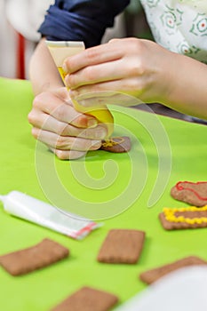 Cinnamon cookies lie on the green table. The hands of the child squeeze yellow frosting out of the tube and create decorations.