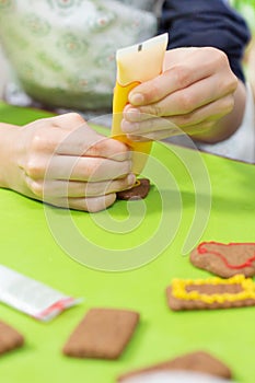 Cinnamon cookies lie on the green table. The hands of the child squeeze yellow frosting out of the tube and create decorations.