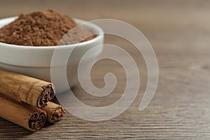 Cinnamon powder and sticks on wooden table, closeup. Space for text