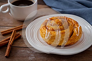 Cinnamon roll bun on white plate and cup of coffee