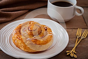 Cinnamon roll bun on white plate and cup of coffee