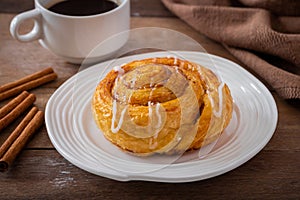 Cinnamon roll bun on white plate and cup of coffee