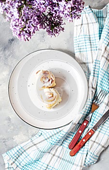 Cinnamon roll or cinnabon with white cream glaze on plate on concrete background. Traditional homemade sweet buns