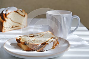 Cinnamon roll or cinnamon bun Dessert on plate with white cup of coffee. sunshine and shadows