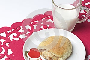 A cinnamon roll lies on a plate. Nearby is a glass of milk. All this on a red openwork napkin.