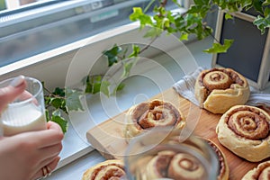 cinnamon rolls on wooden board, person with glass milk, ivy on window ledge