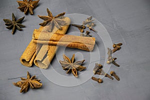 Dried cinnamon  star anise and cloves are scattered on a gray background