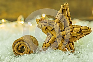 A cinnamon star lies on artificial snow with a string of lights